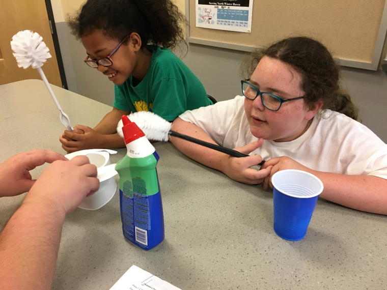 A photo of two girls from our Children's Program with cleaning supplies and cleaning tools.